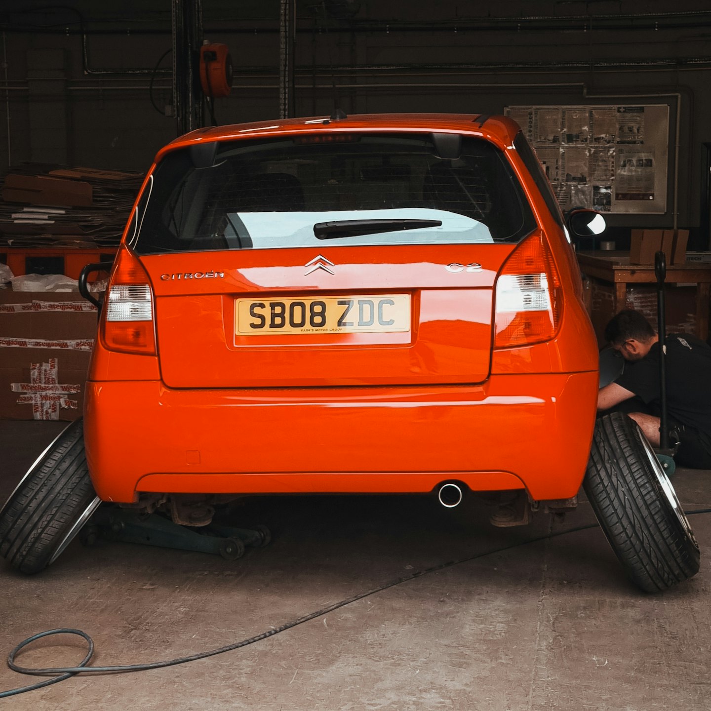 Mechaniker repariert orangenes Auto auf Hebebühne in Werkstatt.