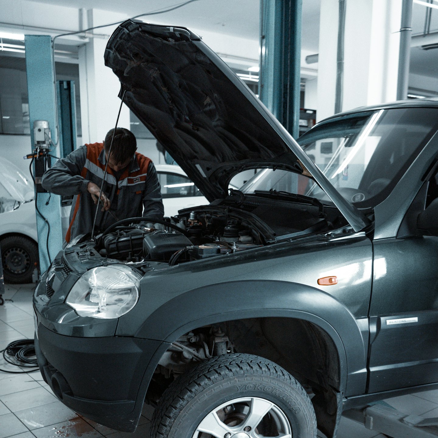Mechaniker in Uniform repariert SUV-Motor in Autowerkstatt.