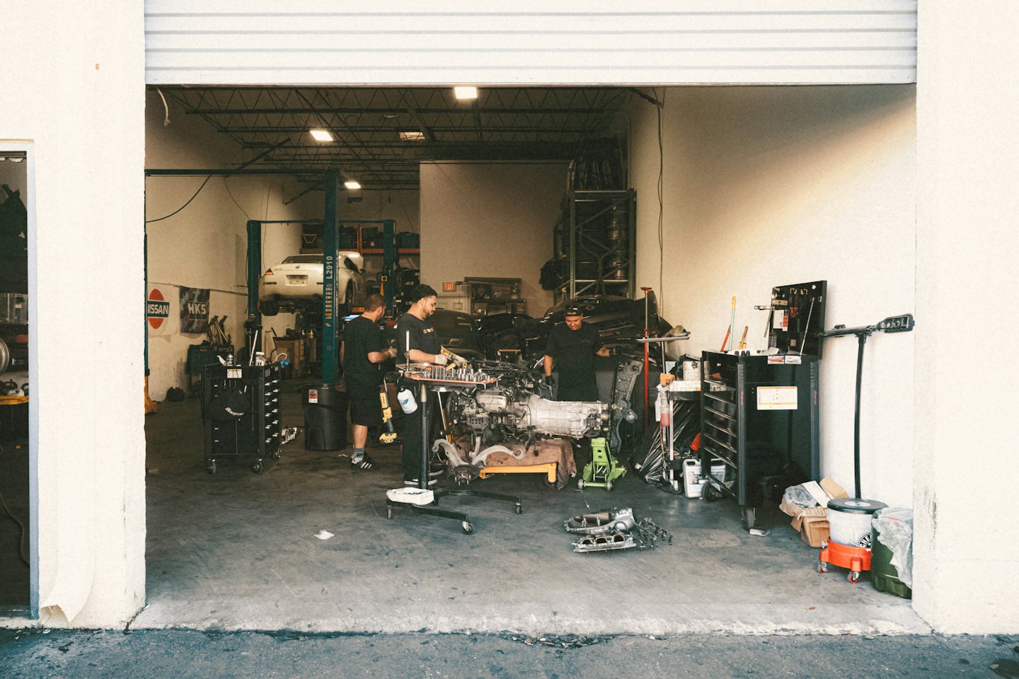 Drei Mechaniker arbeiten gemeinsam an einem Motor in einer Werkstatt.